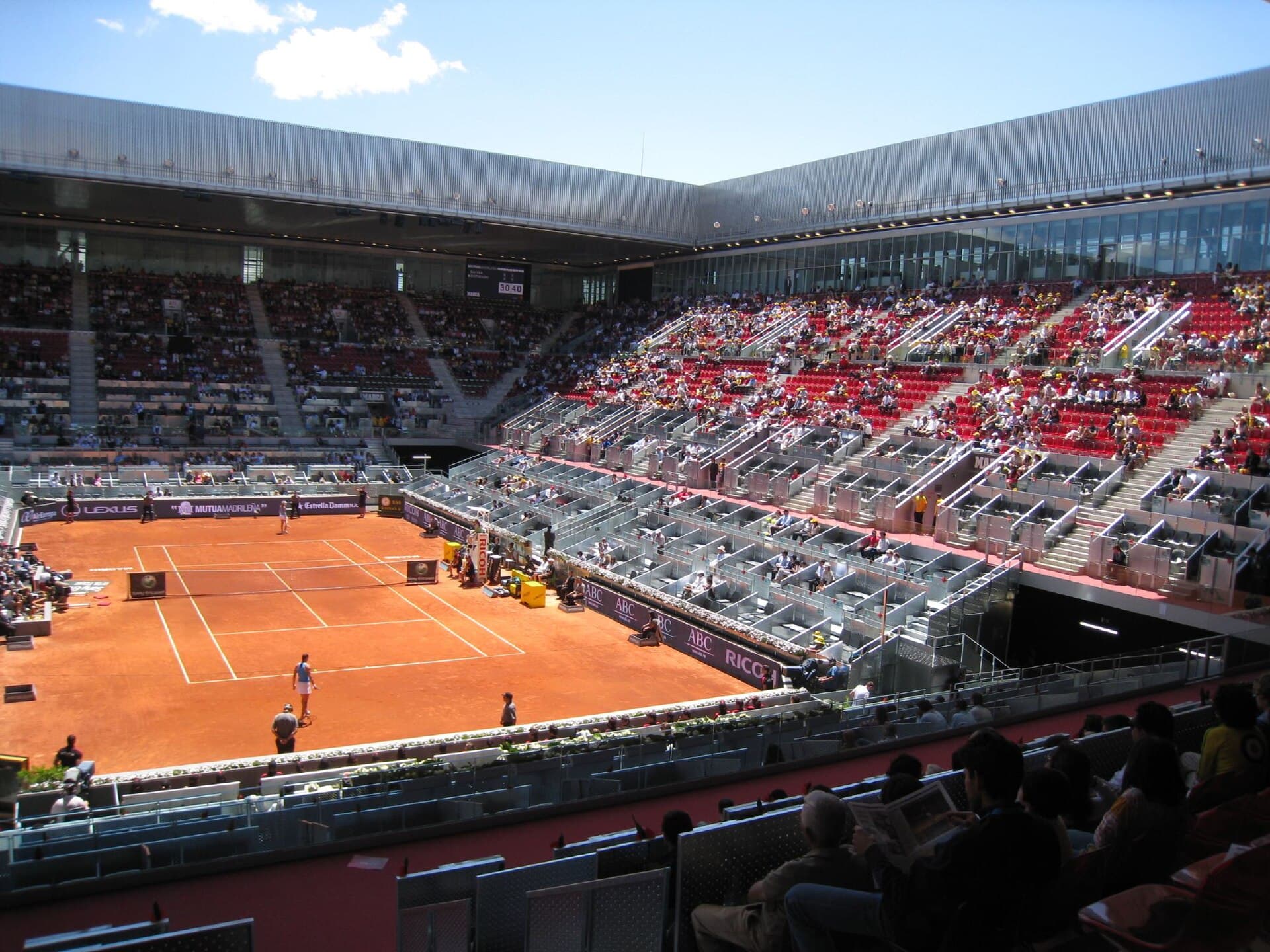 Clay tennis court and tiered red seating inside Madrid’s Caja Magica arena.