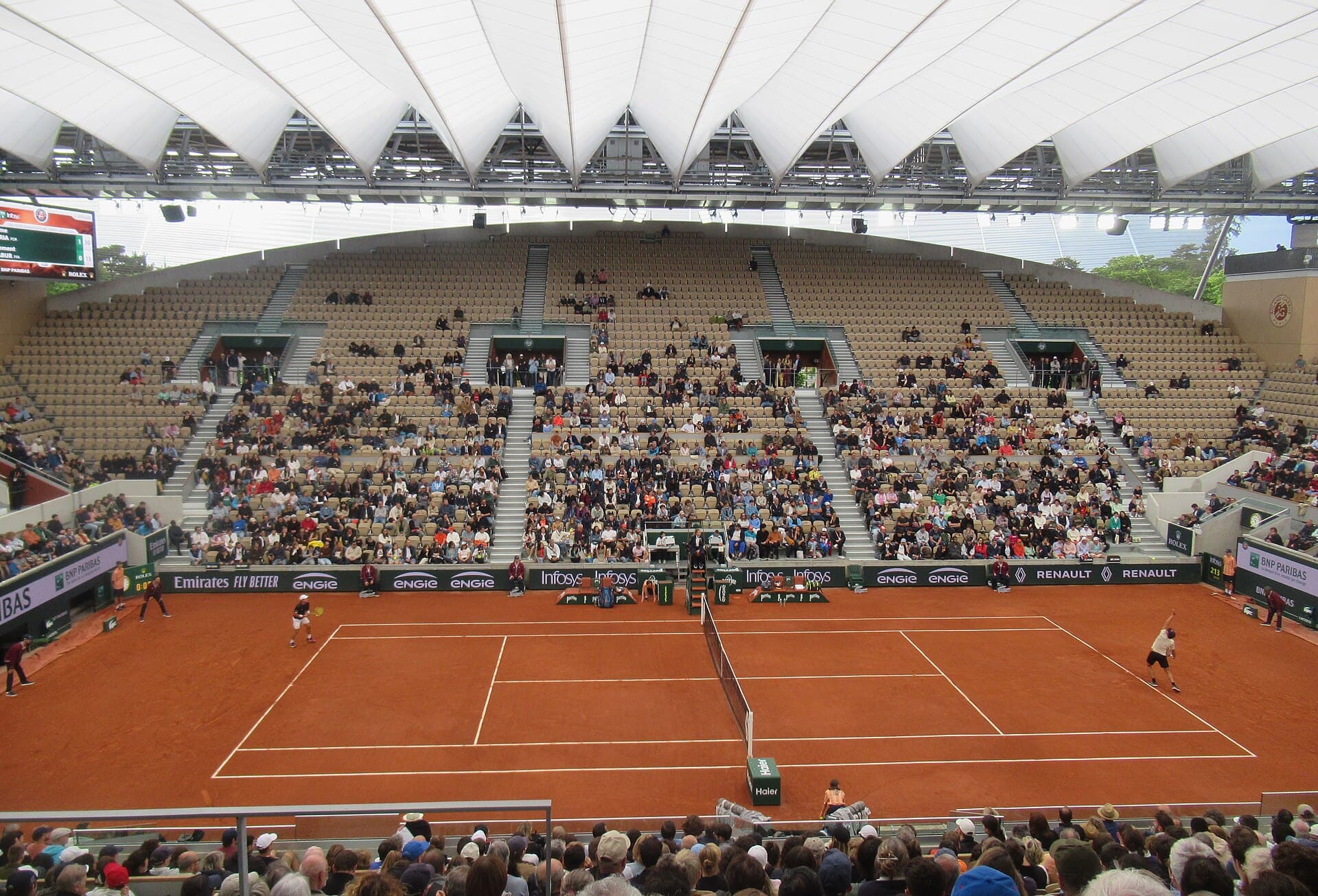 Clay stadium court beneath the sculpted closed roof at Court Suzanne-Lenglen.